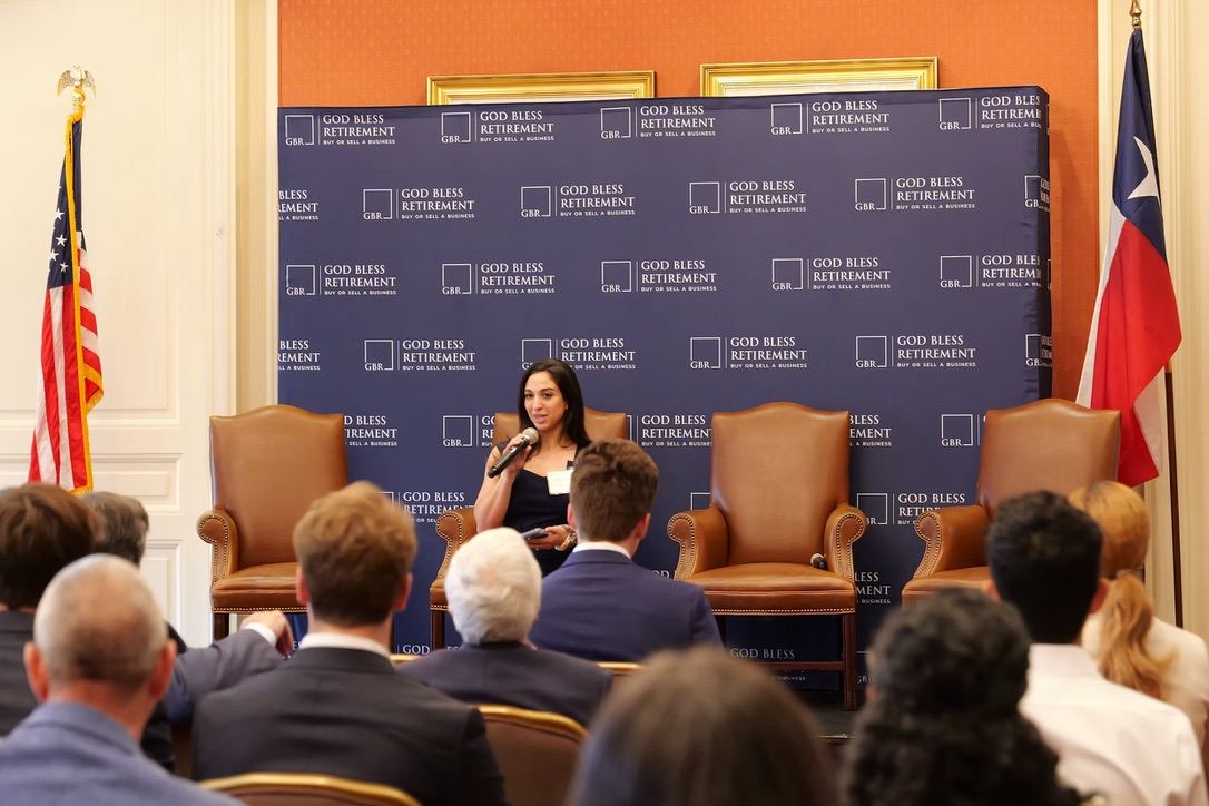 Alexia Tuttle speaking with a microphone in front of a seated audience at a Texas business event.