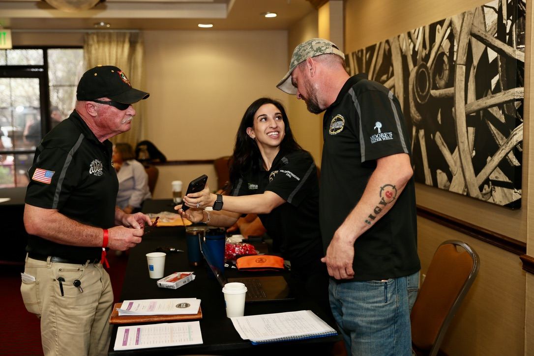 Alexia Tuttle at a registration table talking with two veterans at HALO for Freedom Warrior Week.